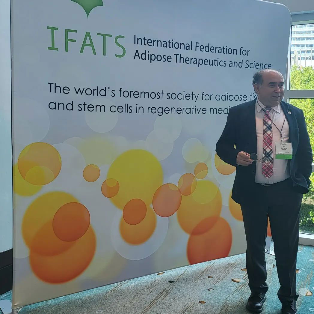 Copcu standing beside the IFATS banner at the International Federation for Adipose Therapeutics and Science meeting