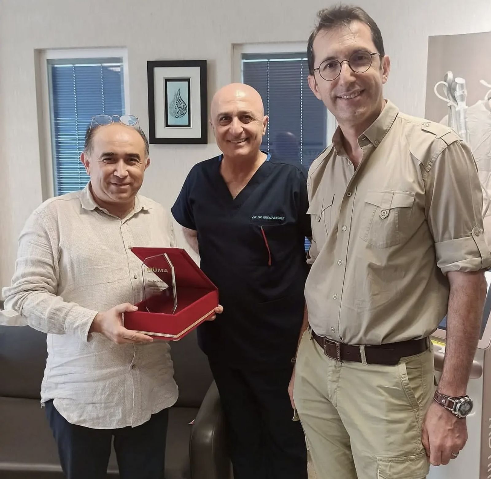 Copcu receiving a commemorative plaque alongside two colleagues in a clinic